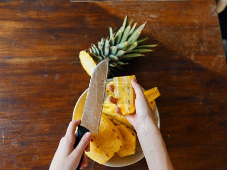 Top view of a ripe pineapple being sliced on a rustic wooden table, showcasing fresh and juicy fruit ready to eat.