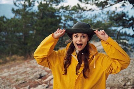 A woman in a yellow raincoat and hat standing triumphantly atop a rugged mountain peak on a daring adventure trip