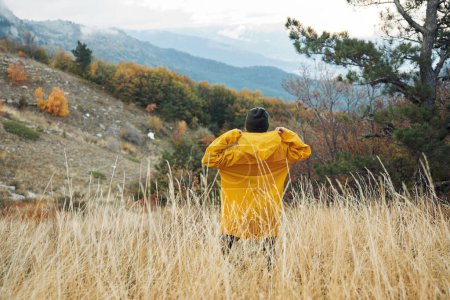 Solitude in the Wilderness A solitary figure in a vibrant yellow raincoat standing amongst the majestic mountains in a vast field