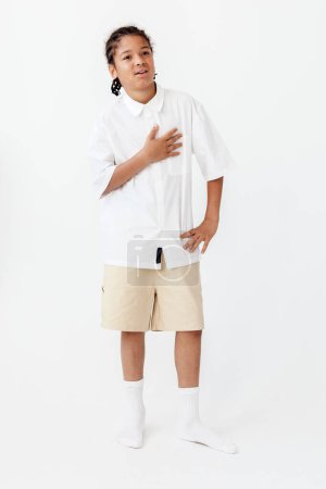 Selbstbewusster kleiner Junge in stylischem Outfit posiert vor schlichtem weißen Hintergrund und strahlt Selbstbewusstsein und Modebewusstsein aus.