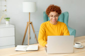 African american girl using laptop at home office looking at screen typing chatting reading writing email. Young woman having virtual meeting online chat video call conference. Work learning from home Poster #643044346