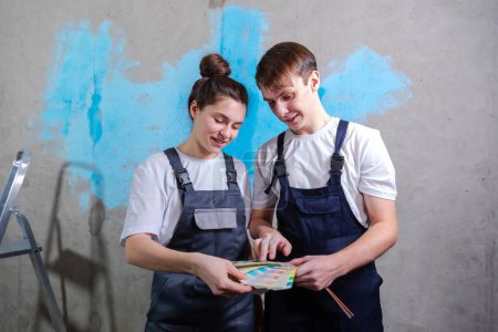 Photo for House decoration DIY renovation concept. Happy couple in empty room of new home planning design. Husband and wife holding swatch palette choosing colors for painting wall in new house - Royalty Free Image