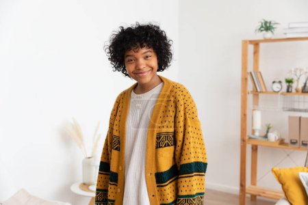 Beautiful african american girl with afro hairstyle smiling at home indoor. Young african woman with curly hair laughing in living room. Freedom happiness carefree happy people concept