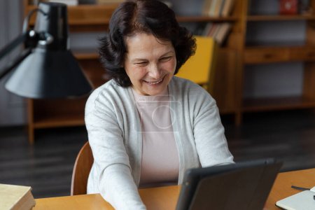 Photo for Happy middle aged senior woman holding tablet talk on video call with friends family. Laughing mature old senior grandmother having fun talking speaking with grown up children online - Royalty Free Image