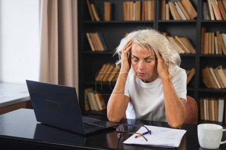 Kopfschmerzen. Frau mittleren Alters berührt Schläfen unter Stress. Ältere alte Dame müde von der Arbeit fühlen Kopfschmerzen krank reiben Schläfen Stirn. Lange Laptop-Nutzung Computer Vision Office-Syndrom