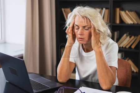 Kopfschmerzen. Frau mittleren Alters berührt Schläfen unter Stress. Ältere alte Dame müde von der Arbeit fühlen Kopfschmerzen krank reiben Schläfen Stirn. Lange Laptop-Nutzung Computer Vision Office-Syndrom