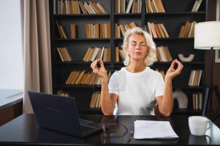 Yoga Mindfulness Meditación Sin estrés mantener la calma. Mujer de mediana edad practicando yoga en la oficina. Mujer tomando un descanso del trabajo meditando relajándose. Señora madura haciendo práctica de respiración en línea yoga en el trabajo