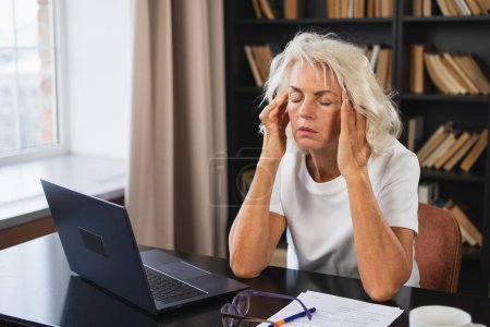 Headache pain. Middle aged woman touching temples experiencing stress. Mature old lady tired of work feeling headache sick rubbing temples forehead. Long laptop usage computer vision office syndrome