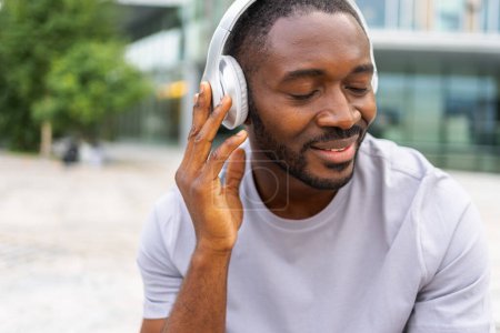 Music song concept. Good start day. Happy African American man listening modern hit on street in city. Person guy wearing headphones enjoy listening favorite music outdoor. People lifestyle joy
