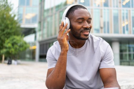 Music song concept. Good start day. Happy African American man listening modern hit on street in city. Person guy wearing headphones enjoy listening favorite music outdoor. People lifestyle joy