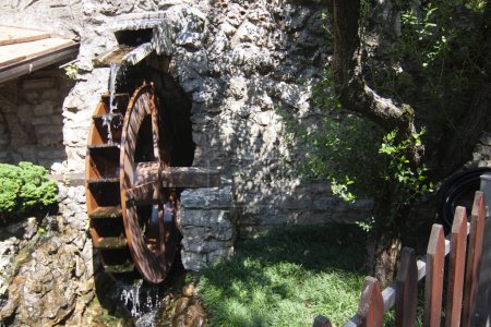 Old water wheel attached to a stone building surrounded by lush foliage