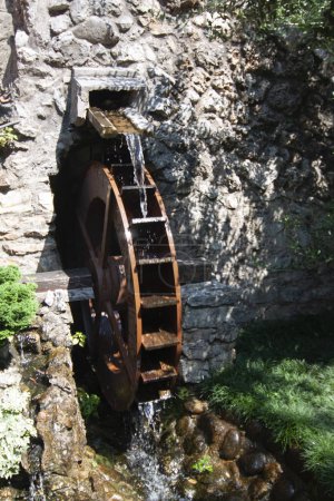 Old water wheel attached to a stone building surrounded by lush foliage