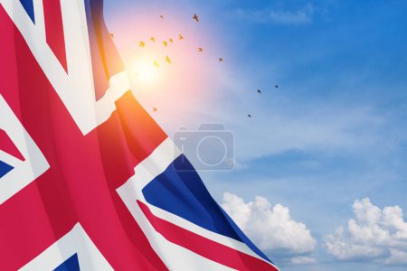Téléchargez les photos : National flags of United Kingdom with flying birds on blue sky background. Background with place for your text. 3d rendering. - en image libre de droit