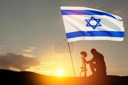 Silhouette eines Soldaten, der mit gebeugtem Kopf und Israel-Flagge gegen den Sonnenaufgang in der Wüste kniet. Konzept - Streitkräfte Israels.