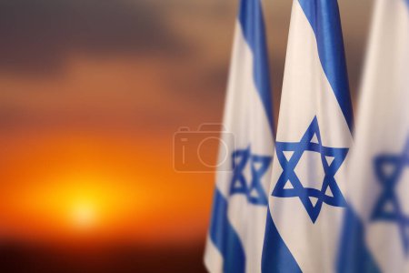 Téléchargez les photos : Israël drapeaux avec une étoile de David sur fond de ciel nuageux sur le coucher du soleil. Concept patriotique sur Israël avec des symboles nationaux de l'État. Bannière avec place pour le texte. - en image libre de droit