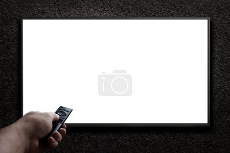 Foto de Televisión en una pared gris oscuro y control remoto en la mano. TV 4K pantalla plana lcd o oled, blanco en blanco HD monitor de maqueta. Panel de vídeo moderno pantalla plana negra. - Imagen libre de derechos