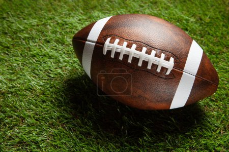 American football ball on green grass field background. Top view.