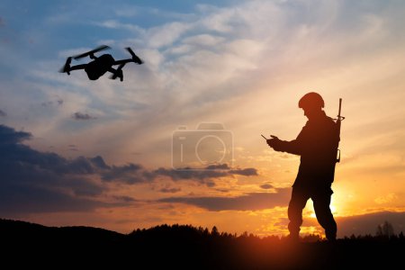 Téléchargez les photos : La silhouette du soldat utilise un drone et un ordinateur portable pour repérer pendant une opération militaire dans le contexte d'un coucher de soleil. Carte de souhaits pour Jour des anciens combattants, Jour du Souvenir, Jour de l'indépendance. - en image libre de droit