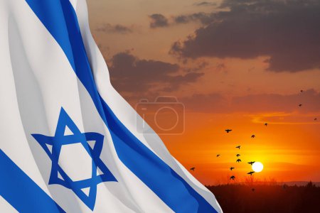 Israel flag with a star of David over cloudy sky background with flying birds on sunset. Patriotic concept about Israel with national state symbols. Banner with place for text.