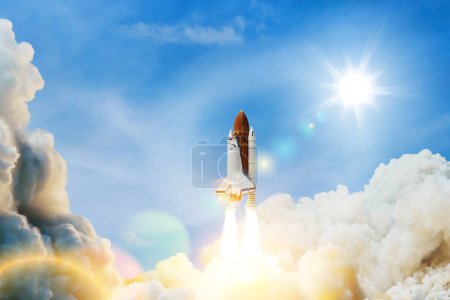 Téléchargez les photos : Spaceship lift off. Space shuttle with smoke and blast takes off into space on a background of blue sky. Successful start of a space mission. Elements of this image furnished by NASA. - en image libre de droit