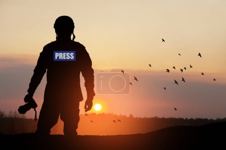 Téléchargez les photos : Silhouette photojournaliste documentant la guerre ou le conflit. Photojournaliste au coucher du soleil. Concept de guerre, armée, technologie et travail de journaliste. - en image libre de droit
