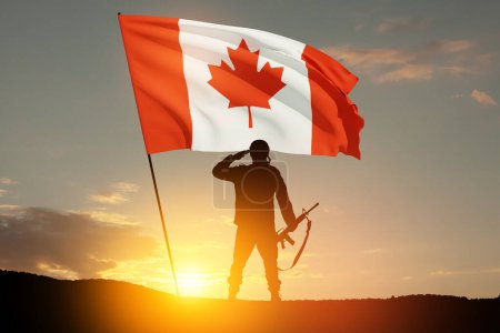 Soldado del ejército de Canadá saludando en un fondo de atardecer o amanecer y bandera de Canadá. Tarjeta de felicitación para el Día de la Amapola, Día del Recuerdo. Celebración en Canadá. Concepto - patriotismo, honor.