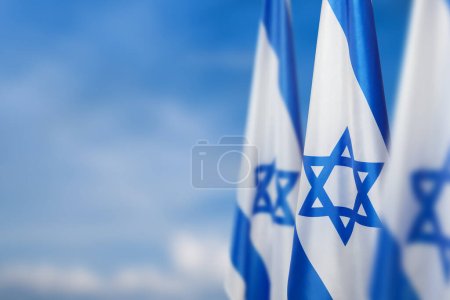 Foto de Israel flags with a star of David over cloudy sky background. Patriotic concept about Israel with national state symbols. Banner with place for text. - Imagen libre de derechos