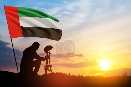 Photo for Silhouette of soldier kneeling with his head bowed against the sunrise or sunset and UAE flag. Concept of national holidays. Commemoration Day. - Royalty Free Image