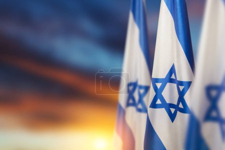 Foto de Israel flags with a star of David over cloudy sky background on sunset. Patriotic concept about Israel with national state symbols. Banner with place for text. - Imagen libre de derechos
