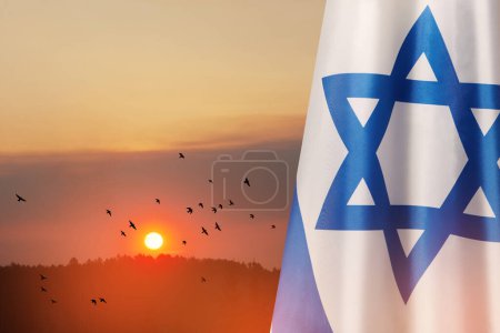 Bandera de Israel con una estrella de David sobre el fondo nublado del cielo con aves voladoras al atardecer. Concepto patriótico sobre Israel con símbolos estatales nacionales. Banner con lugar para texto.