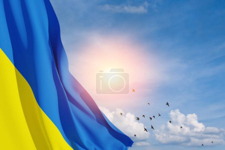Ukraine flag on the blue sky with the sun and flying birds. Close up waving flag of Ukraine with place for your text. Flag symbols of Ukraine. 3d rendering.