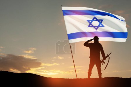 Silhouette eines Soldaten, der mit der israelischen Flagge vor dem Sonnenaufgang in der Wüste grüßt. Konzept - Streitkräfte Israels.