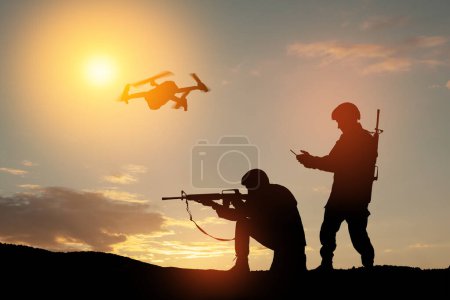 Foto de Silhouettes of soldiers are using drone and laptop computer for scouting during military operation against the backdrop of a sunset. Greeting card for Veterans Day, Memorial Day, Independence Day. - Imagen libre de derechos