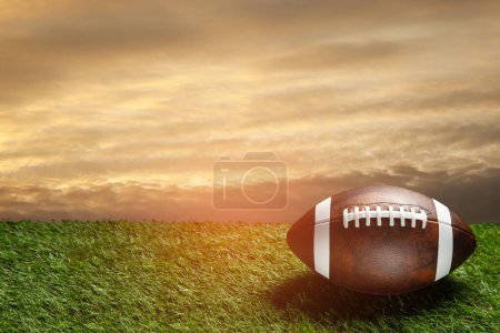 Foto de American football ball on green grass field on background of sunset sky. Banner with space for text. - Imagen libre de derechos