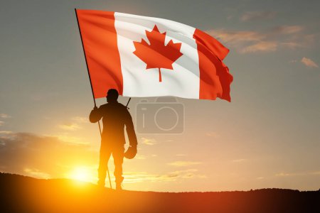 Kanadischer Armeesoldat mit kanadischer Flagge auf einem Hintergrund von Sonnenuntergang oder Sonnenaufgang. Grußkarte zum Mohntag, Gedenktag. Kanada feiert. Konzept - Patriotismus, Ehre.