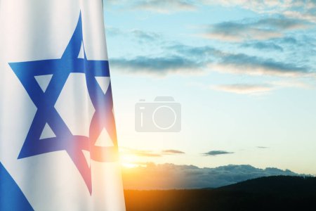 Drapeau d'Israël avec une étoile de David sur fond de ciel nuageux au coucher du soleil. Concept patriotique sur Israël avec des symboles nationaux de l'État. Bannière avec place pour le texte.