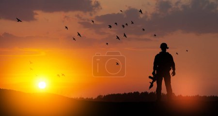 Téléchargez les photos : Silhouette of soldier standing against the backdrop of a sunset. Greeting card for Veterans Day, Memorial Day, Independence Day. USA celebration. Concept - patriotism, protection, remember honor. - en image libre de droit