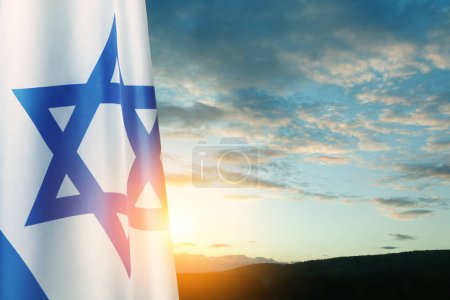 Téléchargez les photos : Drapeau d'Israël avec une étoile de David sur fond de ciel nuageux au coucher du soleil. Concept patriotique sur Israël avec des symboles nationaux de l'État. Bannière avec place pour le texte. - en image libre de droit