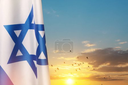 Drapeau d'Israël avec une étoile de David sur fond de ciel nuageux avec des oiseaux volants au coucher du soleil. Concept patriotique sur Israël avec des symboles nationaux de l'État. Bannière avec place pour le texte.
