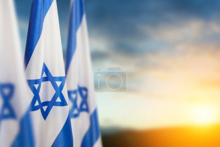 Israel flags with a star of David over cloudy sky background on sunset. Patriotic concept about Israel with national state symbols. Banner with place for text. Poster 653775494