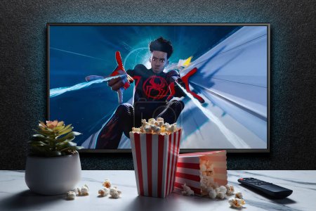 Foto de Pantalla de TV que reproduce Spider-Man a través del tráiler o película de Spider-Verse. TV con control remoto, palomitas de maíz y planta casera. Astana, Kazajstán - 15 de mayo de 2023. - Imagen libre de derechos