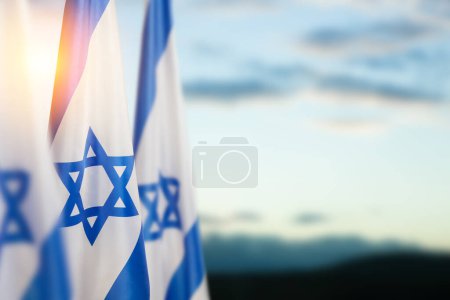 Photo for Israel flags with a star of David over cloudy sky background on sunset. Patriotic concept about Israel with national state symbols. Banner with place for text. - Royalty Free Image
