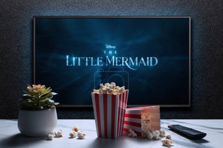 Photo for TV screen playing The Little Mermaid trailer or movie. TV with remote control, popcorn boxes and home plant. Moscow, Russia - March 20, 2023. - Royalty Free Image