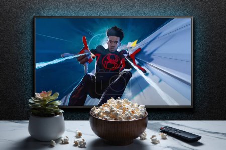 Foto de Pantalla de TV que reproduce Spider-Man a través del tráiler o película de Spider-Verse. TV con control remoto, tazón de palomitas de maíz y planta casera. Astana, Kazajstán - 15 de mayo de 2023. - Imagen libre de derechos