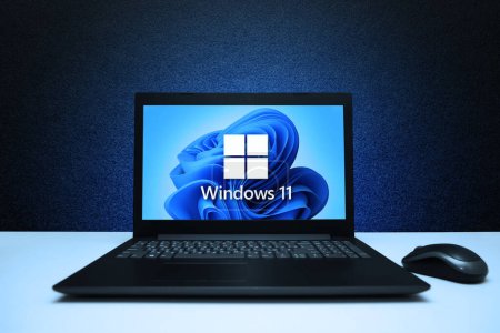 Téléchargez les photos : Logo Windows 11 sur l'ordinateur portable de l'écran avec la souris sur le mur texturé noir avec la lumière bleue. Une nouvelle mise à jour du système d'exploitation de Microsoft. Astana, Kazakhstan - 2 juillet 2023. - en image libre de droit