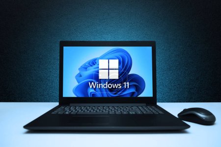 Téléchargez les photos : Logo Windows 11 sur l'ordinateur portable de l'écran avec la souris sur le mur texturé noir avec la lumière bleue. Une nouvelle mise à jour du système d'exploitation de Microsoft. Astana, Kazakhstan - 2 juillet 2023. - en image libre de droit