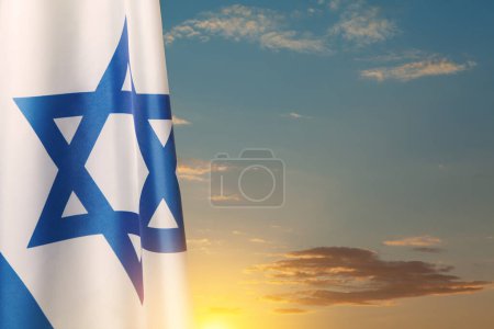 Israel flag with a star of David over cloudy sky background on sunset. Patriotic concept about Israel with national state symbols. Banner with place for text.