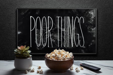 Photo for Poor Things trailer or movie on TV screen. TV with remote control, popcorn bowl and home plant. Astana, Kazakhstan - September 8, 2023. - Royalty Free Image