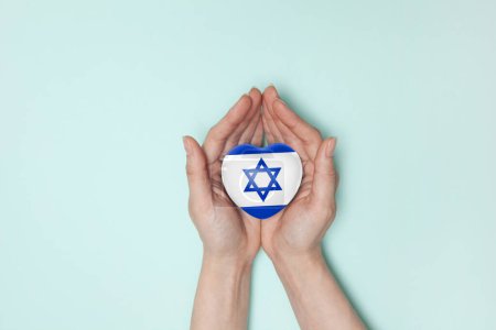 Téléchargez les photos : Coeur avec l'impression du drapeau d'Israël dans les mains des femmes. Pose plate. Espace de copie. - en image libre de droit