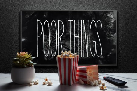 Photo for Poor Things trailer or movie on TV screen. TV with remote control, popcorn boxes and home plant. Astana, Kazakhstan - September 8, 2023. - Royalty Free Image